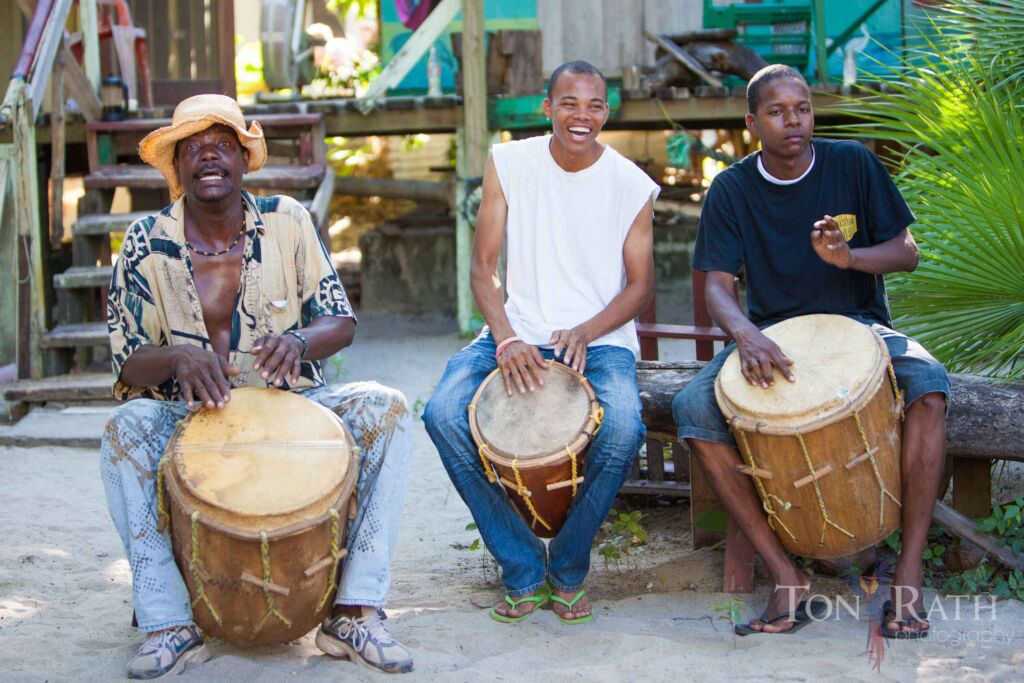Three joyful Garifuna drummers playing traditional drums, smiling and having fun.
